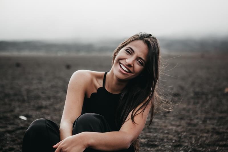 Smiling young woman sitting outdoors on a dark sandy landscape