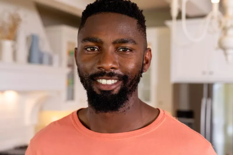 Smiling young man in coral shirt in cozy modern kitchen interior